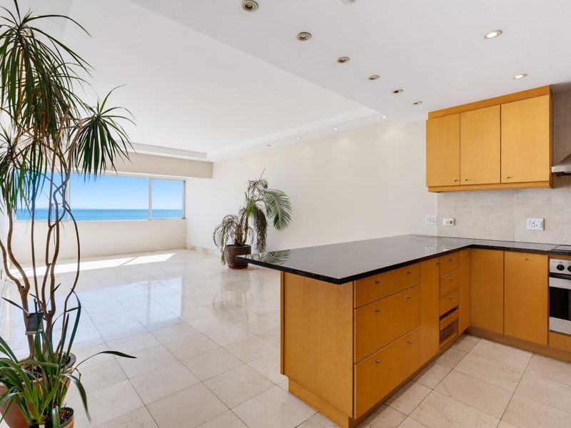 Spacious open-plan living and kitchen area featuring light wood cabinetry, granite countertops, integrated appliances, and large windows with ocean views.