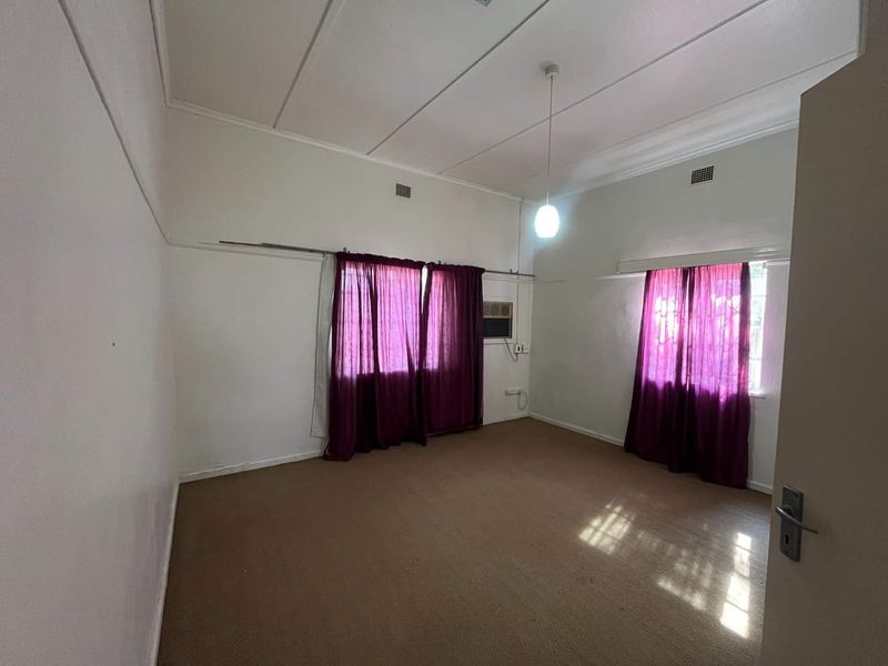 A spacious, empty bedroom featuring carpeted flooring, a built-in air conditioning unit, and classic picture rails, ready for a modern update.