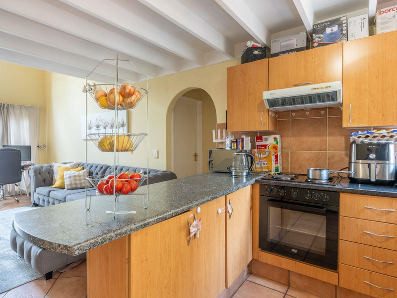Open-plan kitchen and living area featuring wooden cabinetry, granite countertops, built-in oven and hob, tiled floors, and exposed ceiling beams.