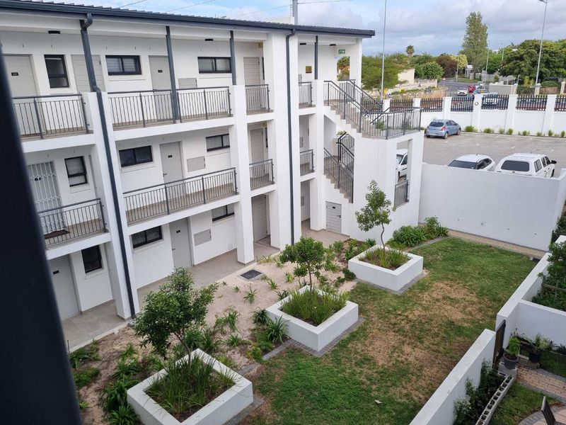 An elevated view of an apartment complex exterior featuring a landscaped courtyard with raised garden beds, metal staircases, and a paved parking area.