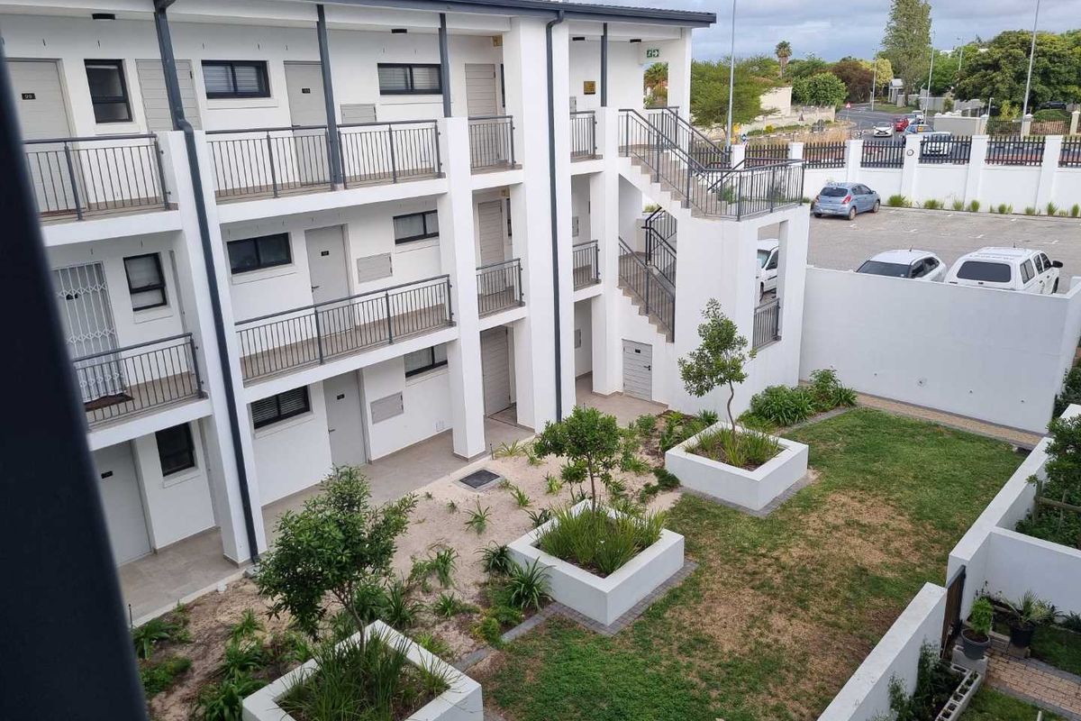An elevated view of an apartment complex exterior featuring a landscaped courtyard with raised garden beds, metal staircases, and a paved parking area.
