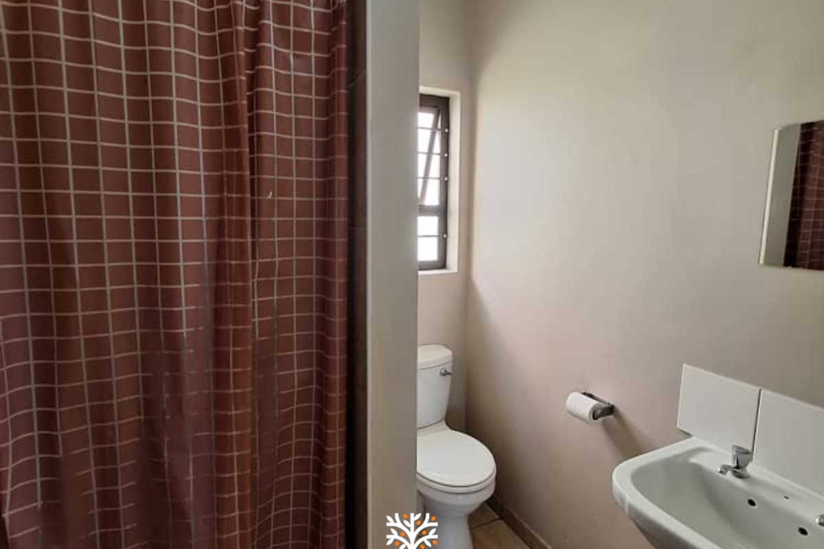 A functional bathroom featuring a pedestal basin, a toilet, and a shower area with a curtain enclosure.