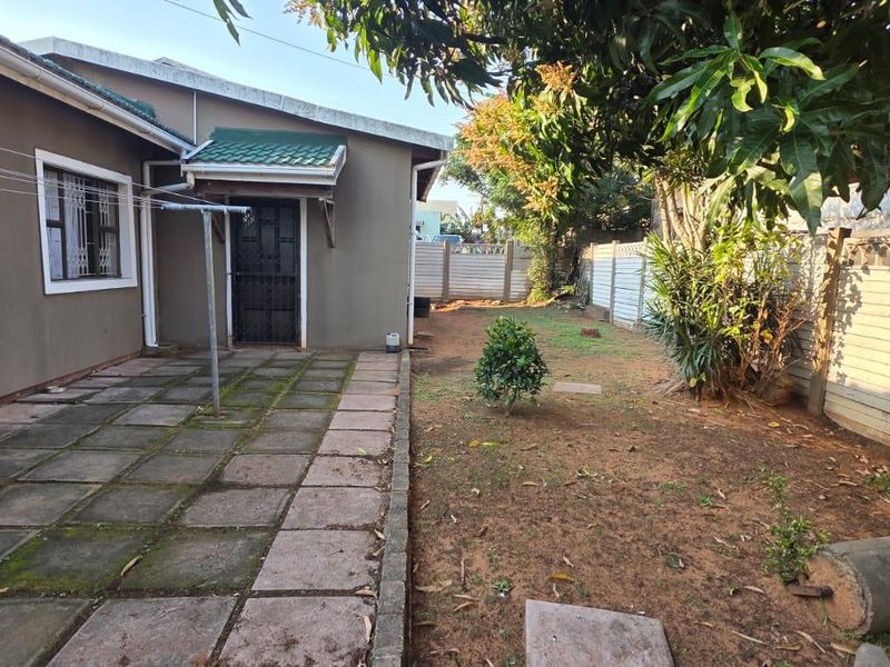 Rear exterior view of the cottage featuring a paved patio area, security gate, and a private garden enclosed by precast concrete boundary walls.