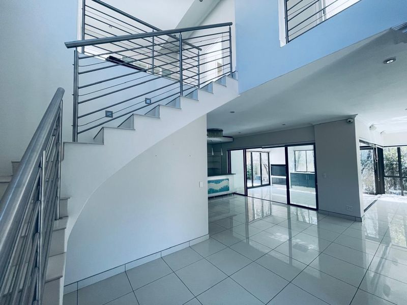 Spacious open-plan living area featuring a modern staircase with stainless steel balustrades, large format floor tiles, and seamless access to the outdoor patio.
