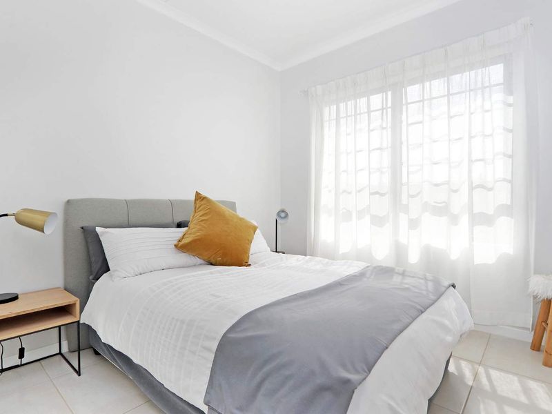A bright and well-maintained bedroom featuring neutral tiled flooring and large windows with installed curtain tracks.