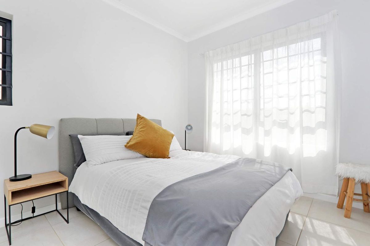 A bright and well-maintained bedroom featuring neutral tiled flooring and large windows with installed curtain tracks.