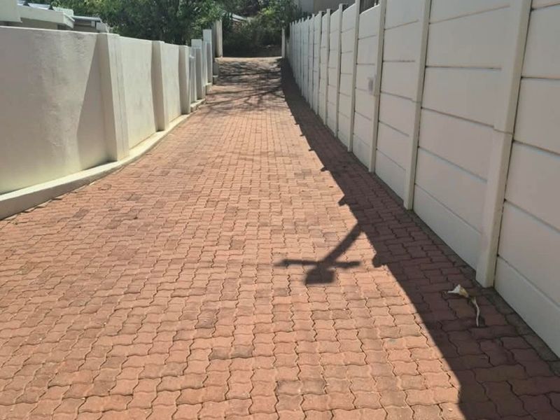 A paved driveway leading towards the property entrance, enclosed by secure precast concrete boundary walls.