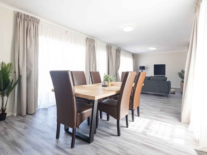 Spacious open-plan living and dining area featuring modern light-toned laminate flooring and abundant natural light through large windows.