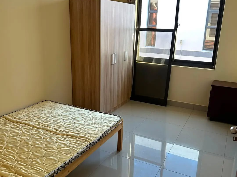 A bright bedroom featuring polished tiled flooring, neutral walls, and a large sliding window providing natural light.