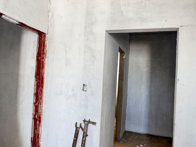 An interior hallway space currently under construction, featuring unfinished plastered walls and exposed door frames, offering a blank canvas for renovation.