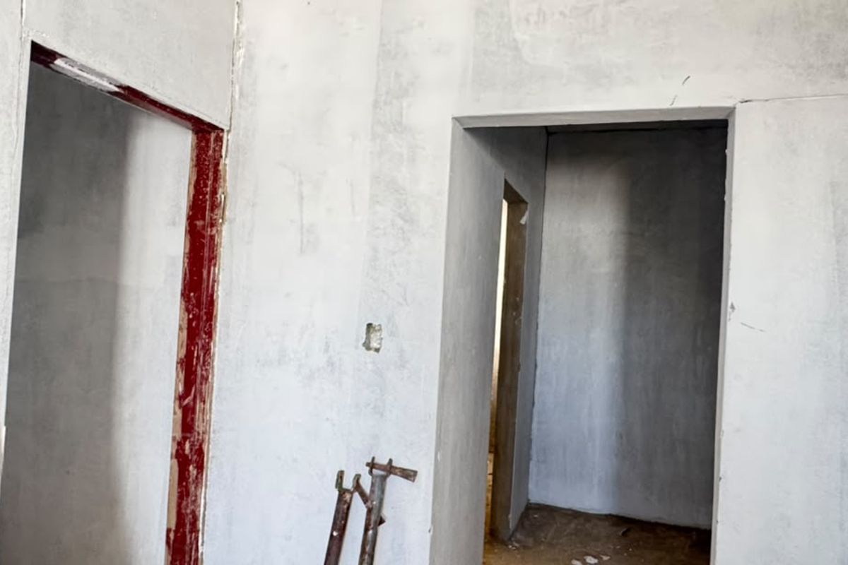 An interior hallway space currently under construction, featuring unfinished plastered walls and exposed door frames, offering a blank canvas for renovation.