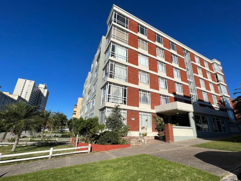 Exterior view of the Arusha apartment building featuring a red brick facade, large windows, and a paved entrance area.
