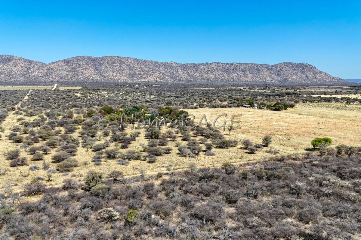 An aerial view of a large rural small holding featuring expansive natural landscape, scrub vegetation, and distant mountain views.