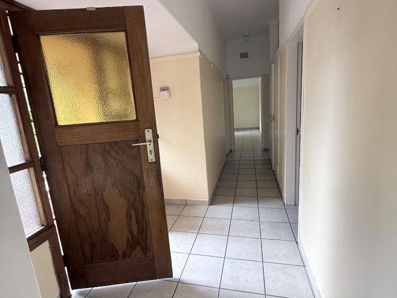 A long, tiled hallway featuring a traditional timber door with textured glass panels, leading through to the interior living spaces of the home.