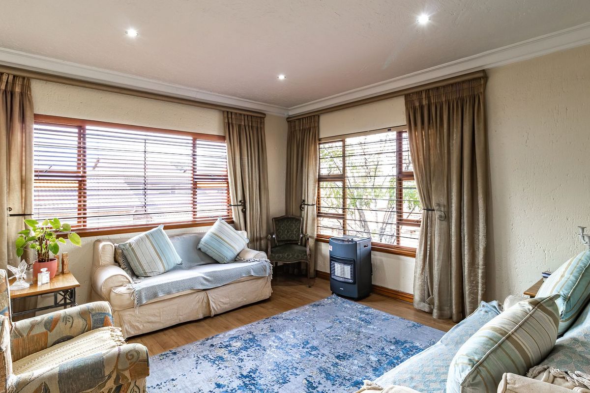 A comfortable living room featuring timber laminate flooring, recessed downlighting, and large windows with timber frames, offering a bright and inviting atmosphere.