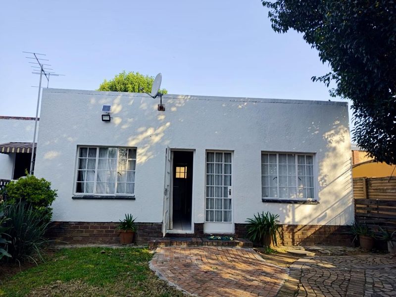 Rear exterior view of a cottage featuring a white stucco facade, brick plinth, steel-framed windows, and a paved pathway leading to the entrance.