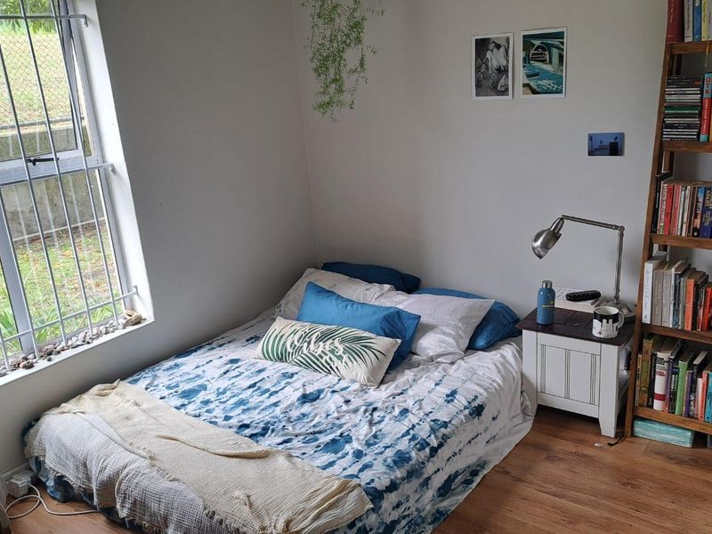 A compact bedroom featuring laminate flooring and a window with security bars, providing natural light and a view of the exterior area.