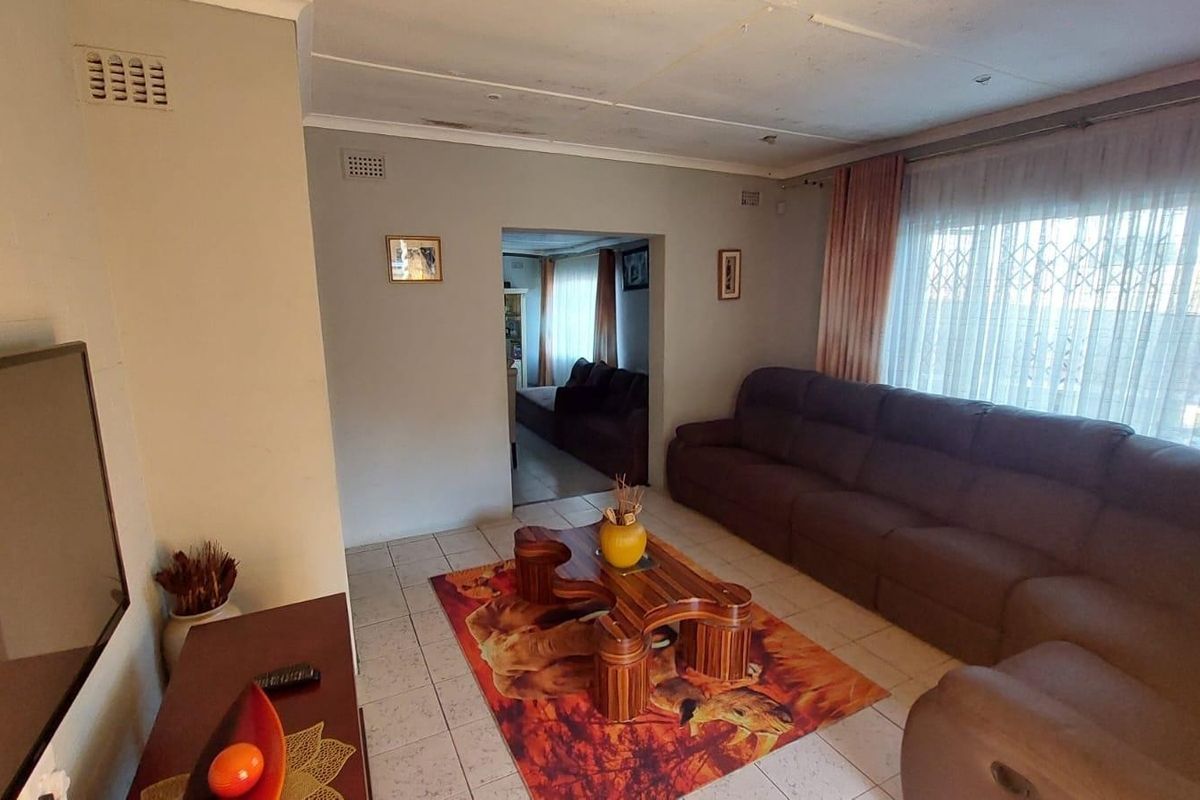 A living room featuring tiled flooring and large windows with security gates, showing signs of ceiling wear and water damage.