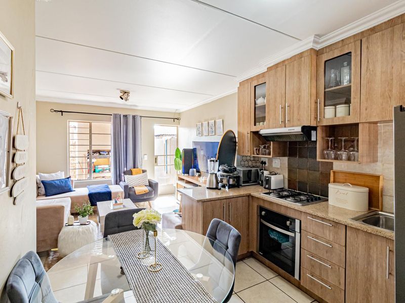 An open-plan living and kitchen area featuring wood-finish cabinetry, granite countertops, built-in appliances, and tiled flooring with access to an outdoor space.