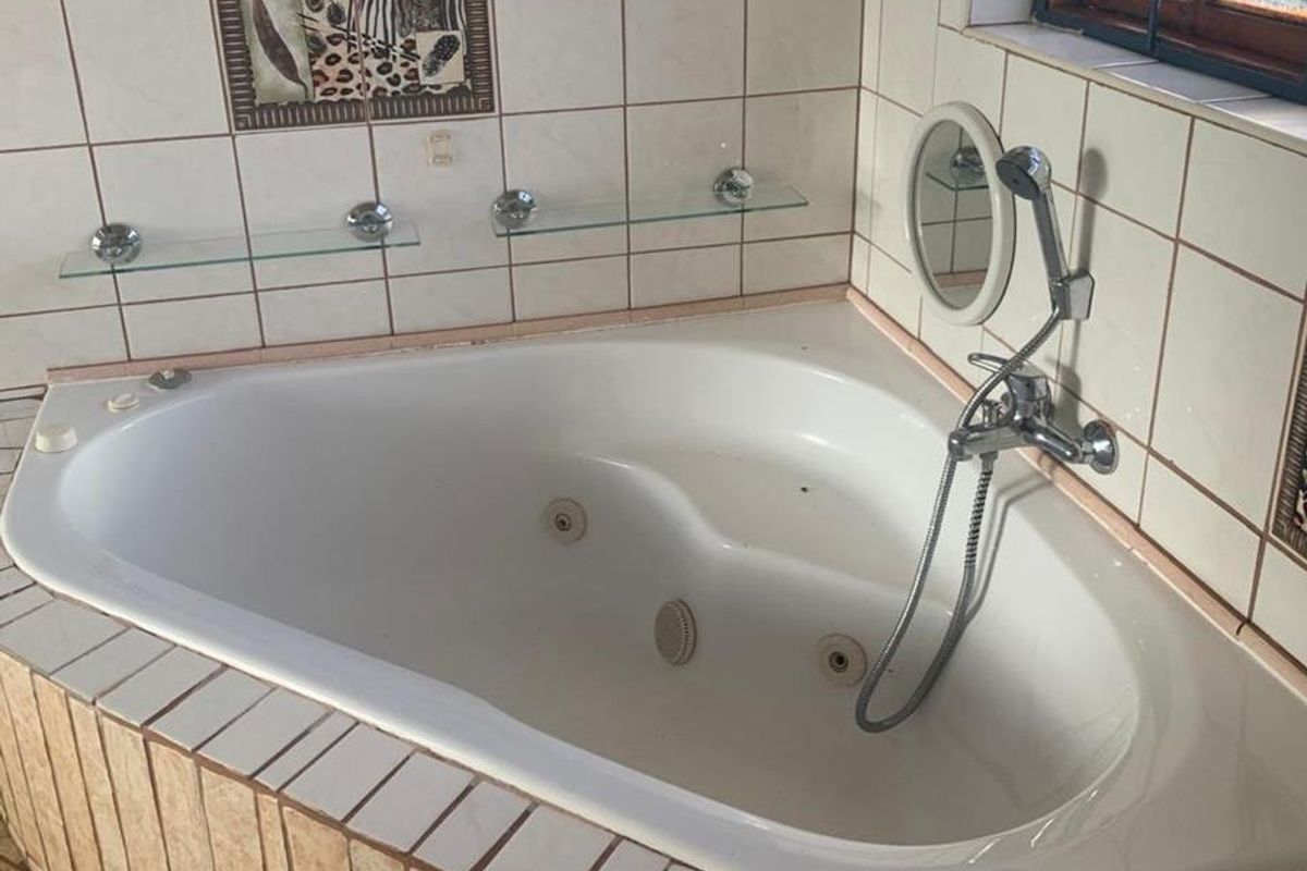 A bathroom featuring a corner spa bath with handheld shower mixer, tiled surround, and decorative wall tiling.