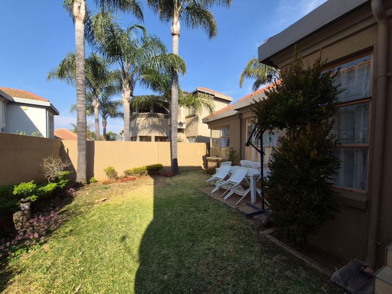 A private rear garden featuring a paved patio area, established palm trees, and a secure boundary wall, offering a pleasant outdoor space.