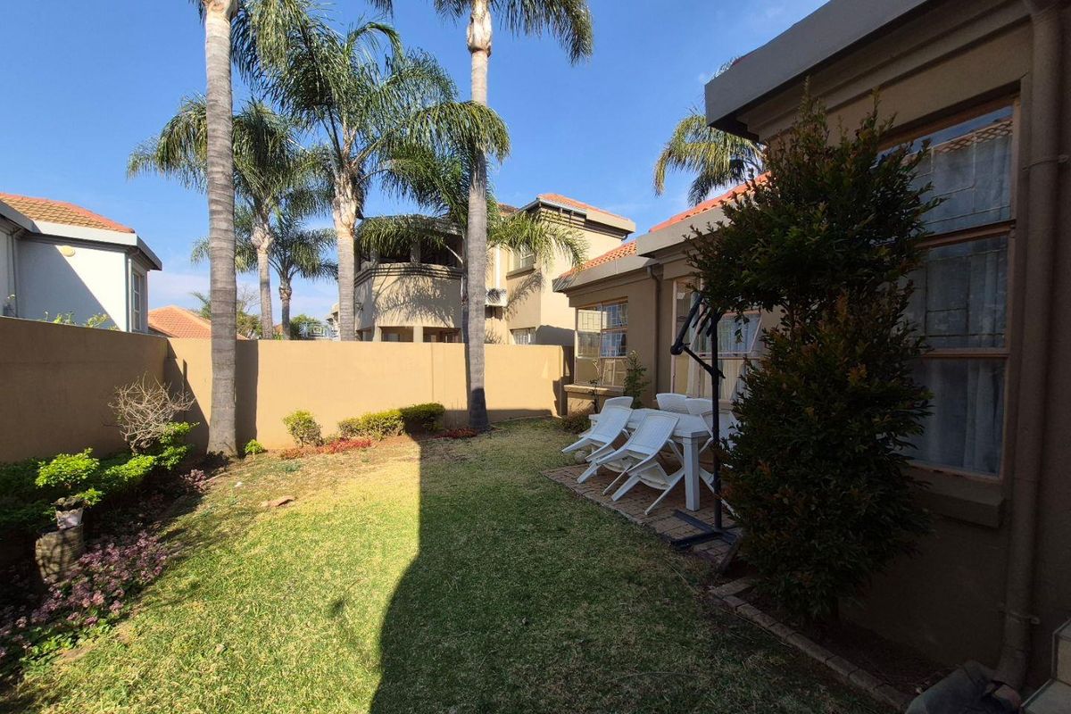 A private rear garden featuring a paved patio area, established palm trees, and a secure boundary wall, offering a pleasant outdoor space.