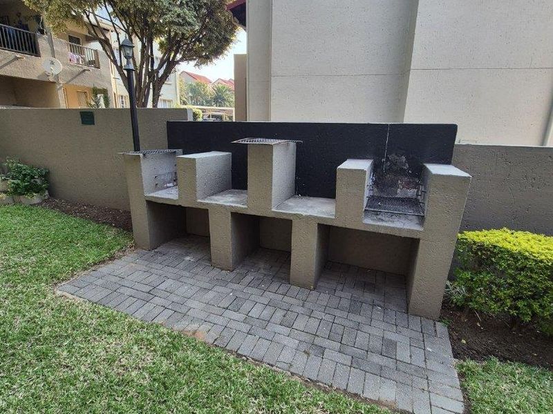 A communal garden area featuring a large, built-in masonry braai station set on a paved base within the apartment complex grounds.