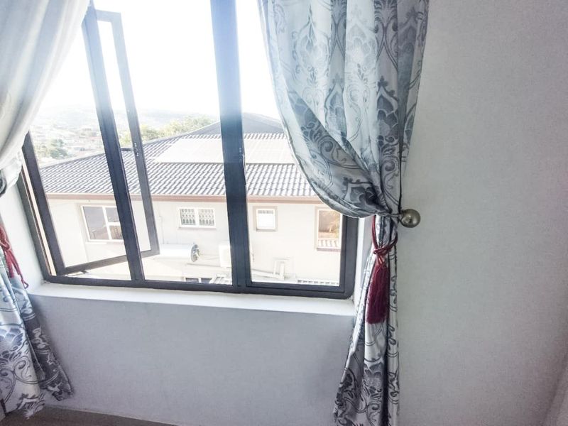 A bedroom interior featuring a large aluminium-framed window with a view of the surrounding residential area.