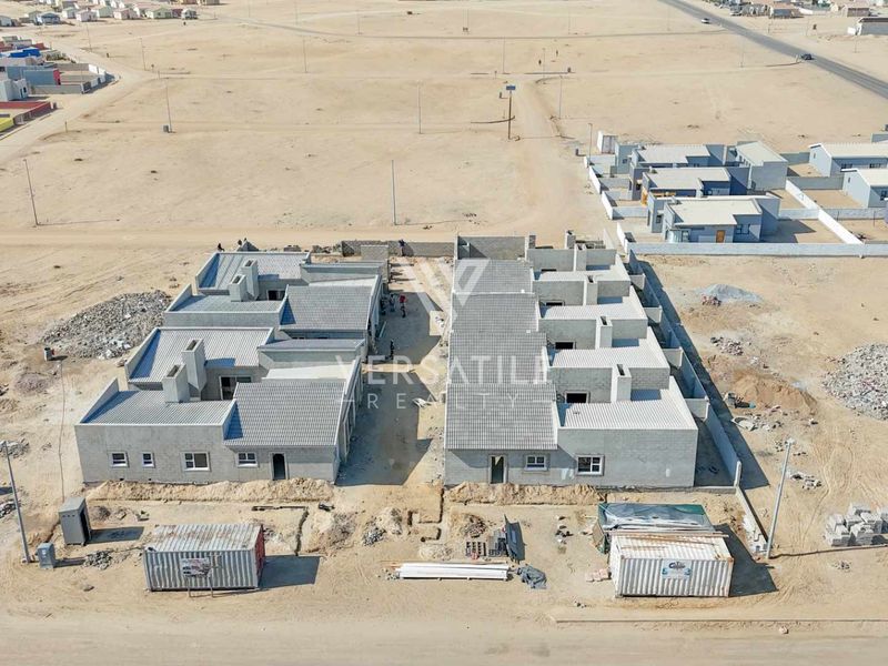 Aerial view of a townhouse development under construction, showing multiple units with tiled roofs and masonry walls in a developing residential area.