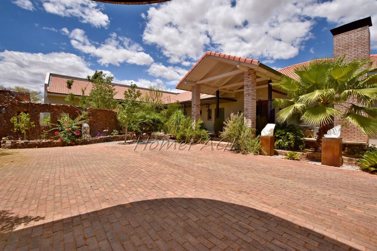 A spacious paved courtyard area featuring a covered patio entrance, brick masonry, and established garden landscaping.