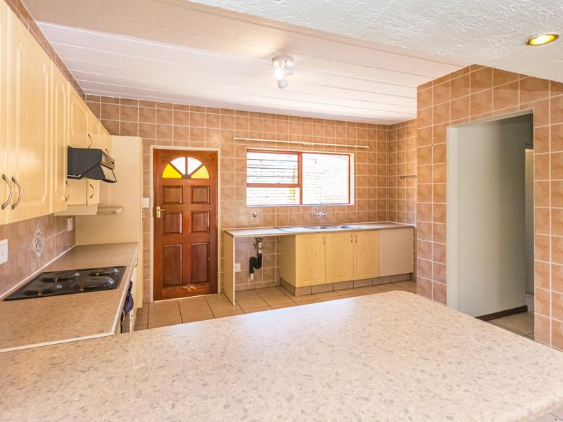 A functional kitchen featuring built-in cabinetry, laminate countertops, an electric hob, and tiled finishes throughout, offering a blank canvas for potential modern updates.