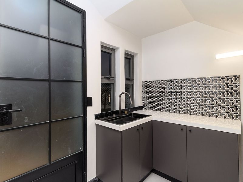 Modern scullery featuring sleek dark cabinetry, stone countertops, a patterned tile splashback, and a stylish steel-framed glass door with ample natural light.