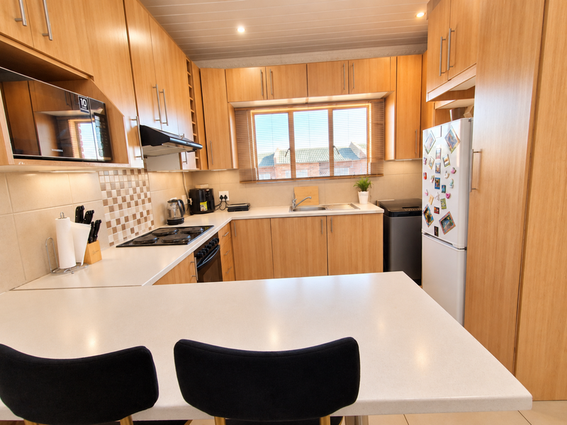 A well-maintained kitchen featuring light wood cabinetry, laminate countertops, a built-in oven, electric hob, and a breakfast bar area.