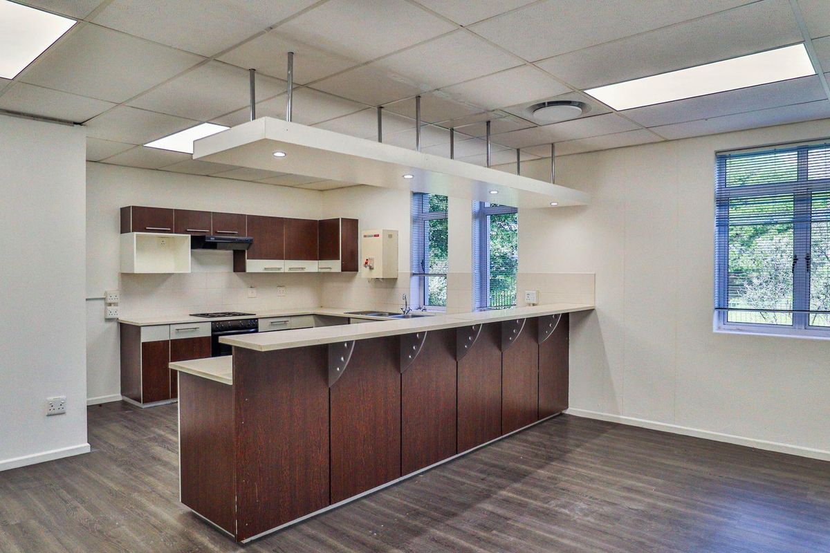 A functional office kitchenette featuring dark wood cabinetry, a breakfast bar, integrated stove, and recessed ceiling lighting in a clean, open-plan workspace.