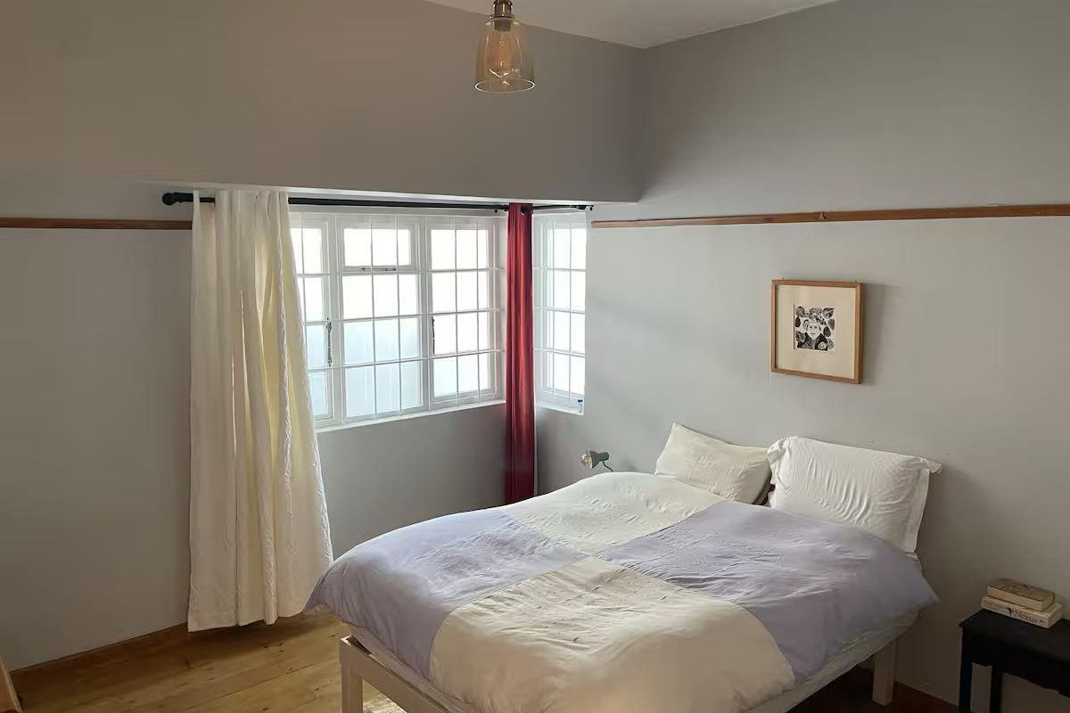 A bedroom featuring natural wooden flooring, a large multi-pane window, and a pendant light fixture.