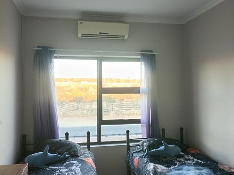 A functional bedroom featuring tiled flooring, a split-system air conditioner, and a large window providing natural light and exterior views.