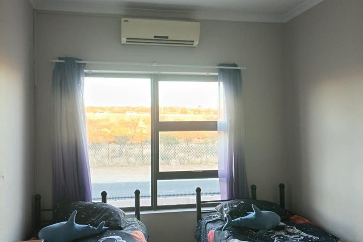 A functional bedroom featuring tiled flooring, a split-system air conditioner, and a large window providing natural light and exterior views.