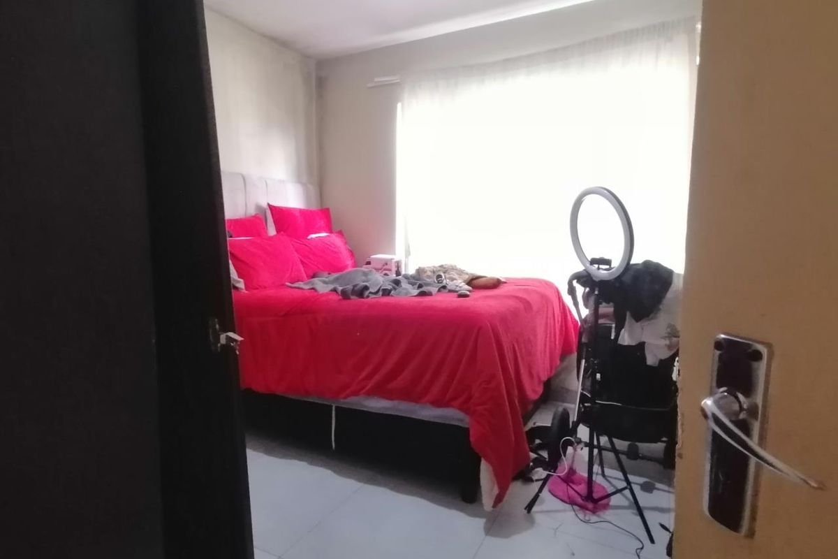 A bedroom featuring tiled flooring and a window with sheer curtains, viewed from the doorway.