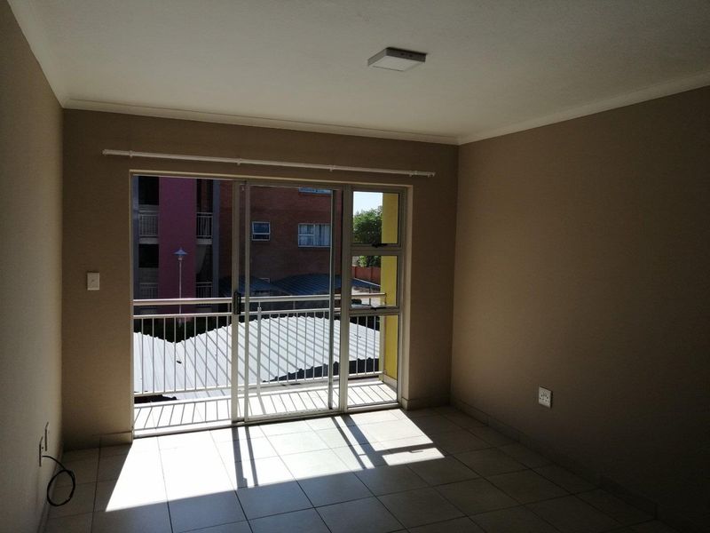 An empty living room featuring tiled flooring and a large sliding glass door providing access to a balcony.