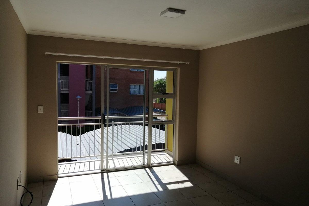 An empty living room featuring tiled flooring and a large sliding glass door providing access to a balcony.