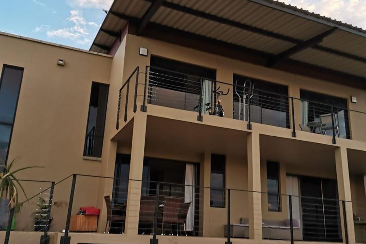 Rear elevation of a modern townhouse featuring a double-story design with balconies, cable railings, and a paved patio area.