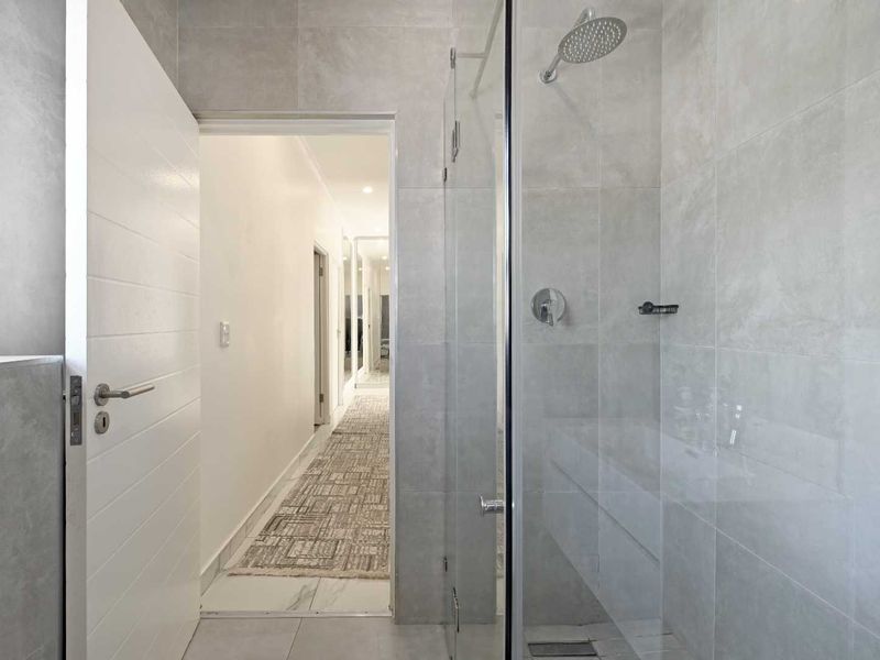 Modern bathroom featuring a walk-in shower with glass screen and contemporary grey tiling, leading into a bright hallway.