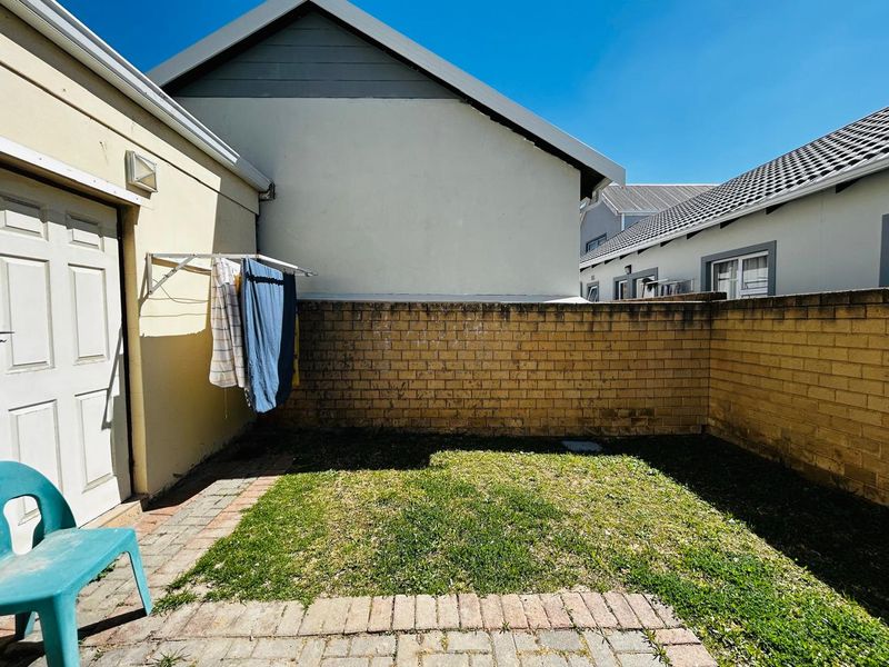 A private rear courtyard featuring a paved patio area, a small lawn, and a brick boundary wall with a wall-mounted clothesline.