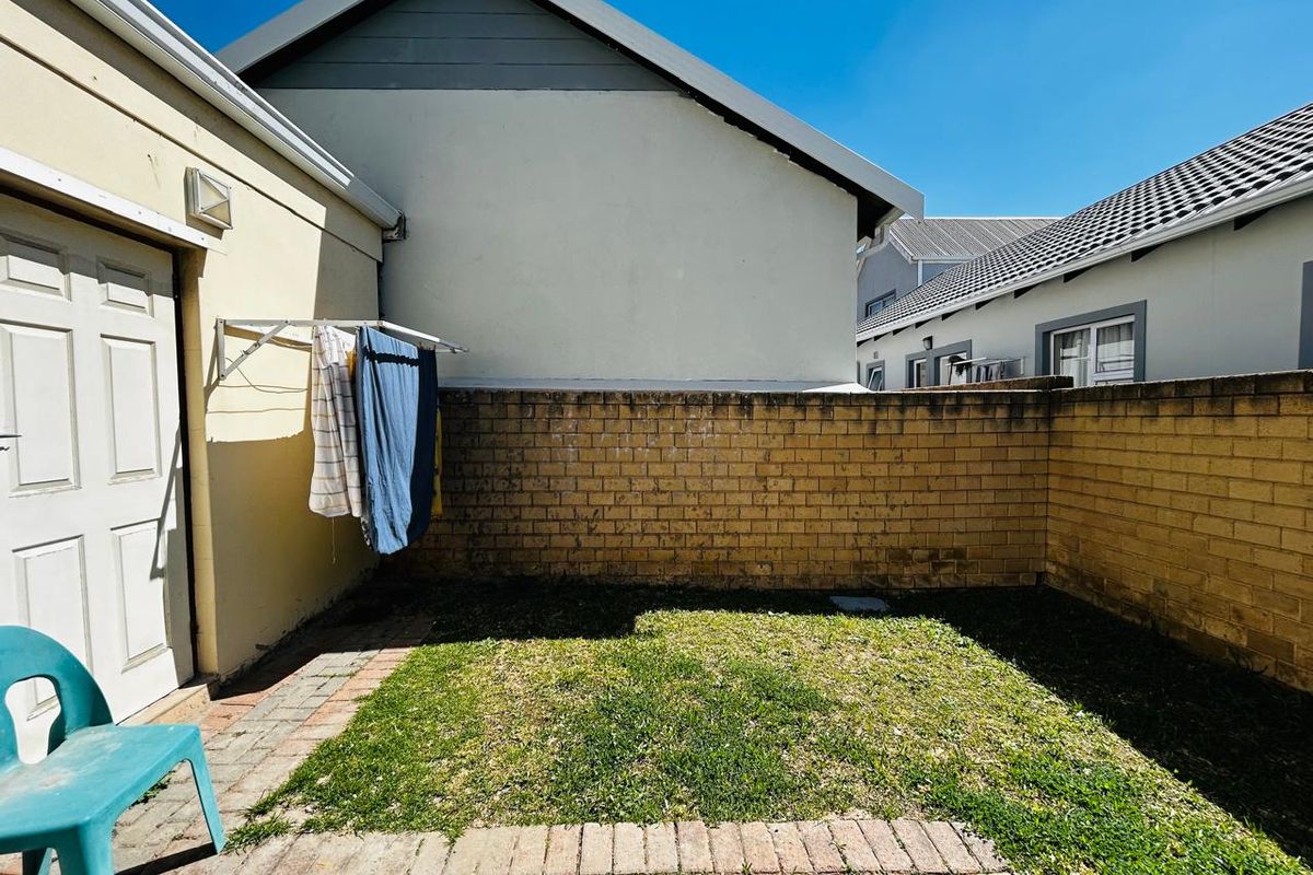 A private rear courtyard featuring a paved patio area, a small lawn, and a brick boundary wall with a wall-mounted clothesline.
