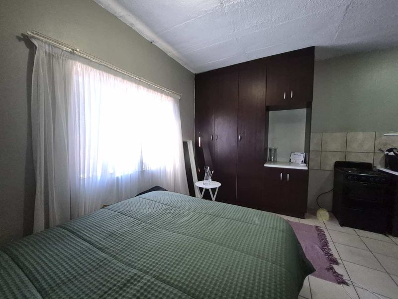 A bedroom featuring built-in dark wood cupboards, tiled flooring, and a stove, indicating a studio-style layout with visible ceiling wear.