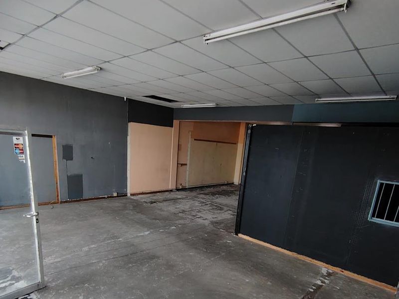 An empty, open-plan commercial space featuring a suspended ceiling, fluorescent lighting, and exposed concrete flooring, suitable for various business or retail fit-out opportunities.