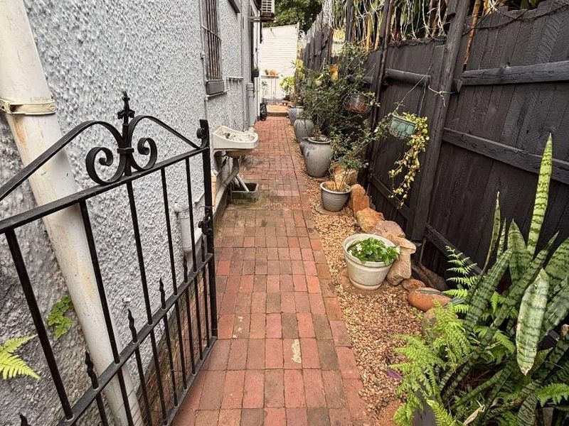 A narrow side passage featuring brick paving, a wrought iron gate, and a wall-mounted utility basin along the exterior wall.