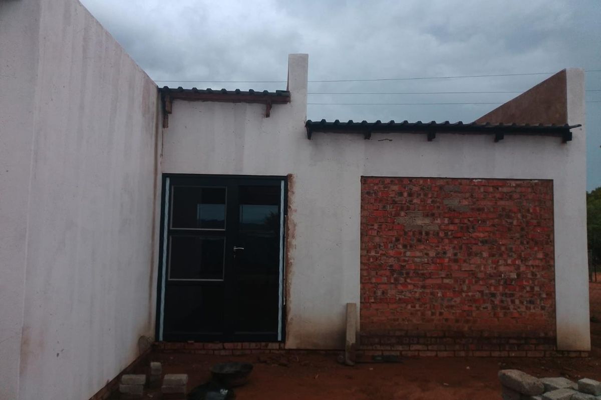 Exterior view of a property under construction, featuring an installed black frame glass door and unfinished brickwork sections.