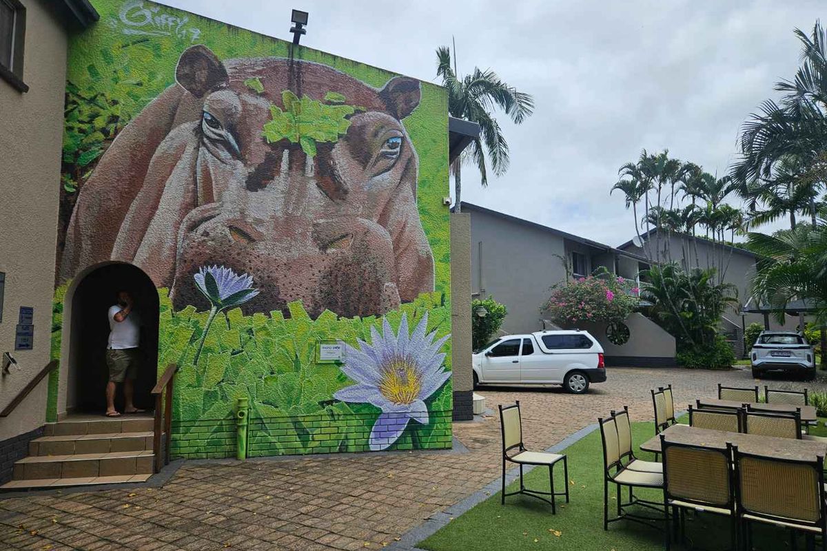 A communal outdoor courtyard area featuring a large decorative mural on the building facade, paved flooring, and access to the apartment entrance.