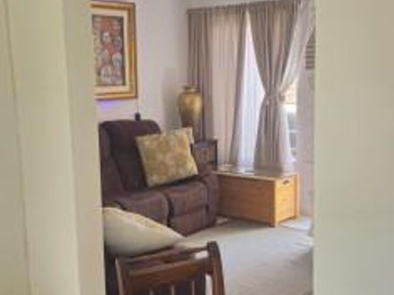 A view into a living room area featuring tiled flooring and ceiling-mounted lighting, viewed through an arched doorway from an adjacent space.
